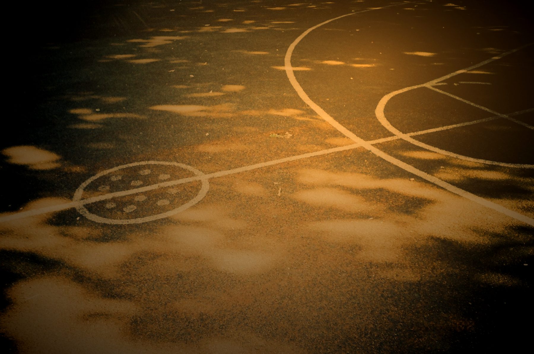 Sunlight and shadow across the painted lines of an empty outdoor court